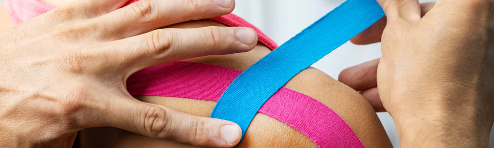 Kinesio taping being done on a young woman's shoulder